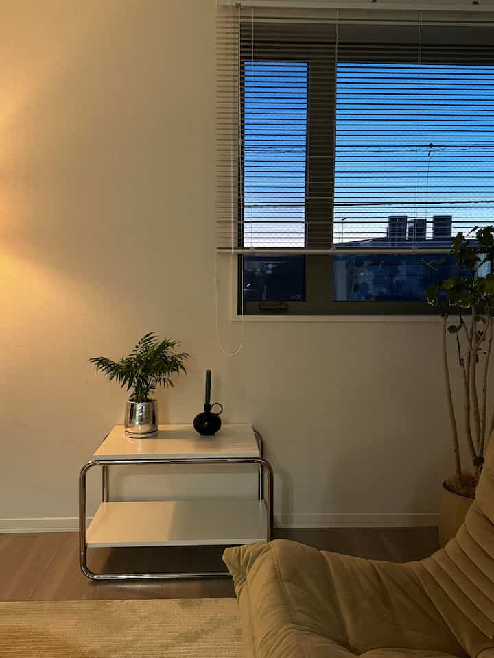 A natural-toned living room with white walls and wood flooring, featuring a beige sofa and white side table creating a cozy atmosphere
