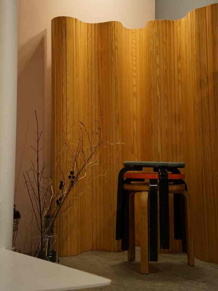 Warm wood tone corner featuring Artek stools and wooden Aalto screen in a Nordic style entrance-adjacent space
