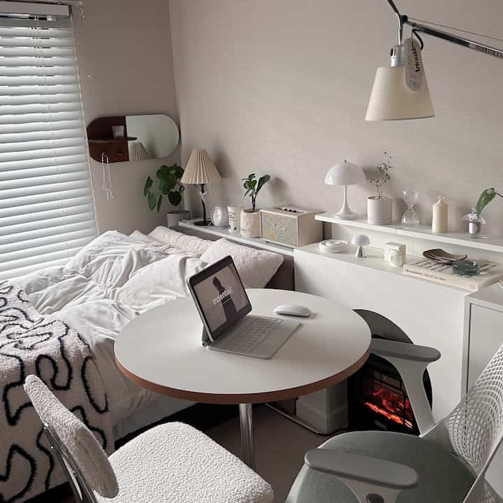 ホワイトとウッドトーンが調和したコンパクトな寝室、窓際に置かれたベッドと丸テーブルのある自然なモダンなインテリア