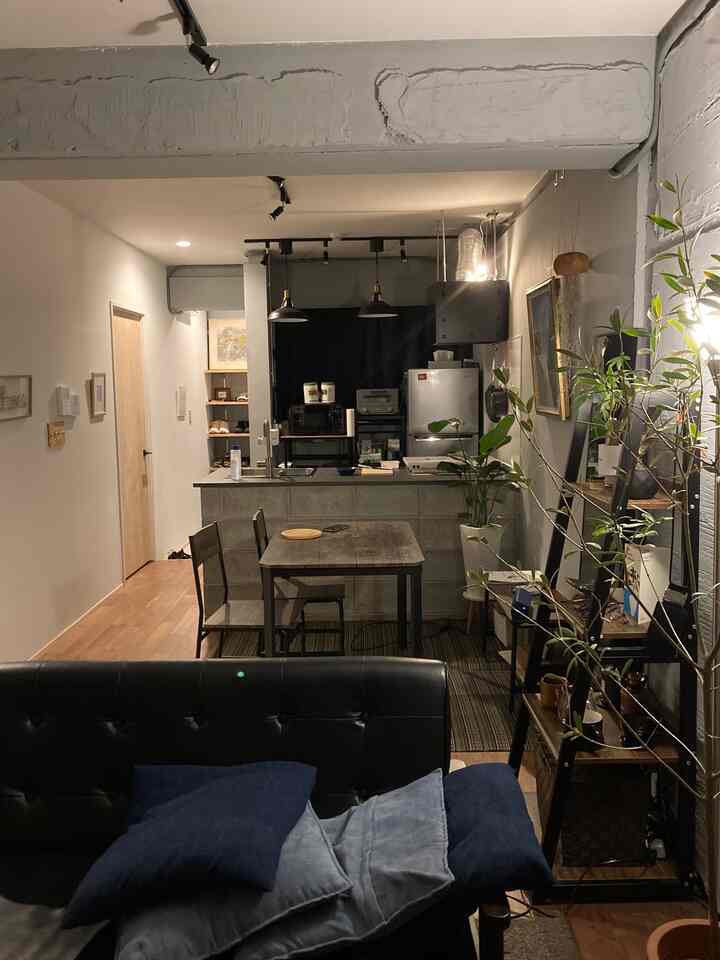 黒・グレー・茶色のトーンのダイニング兼リビングスペース、木製のダイニングテーブルとソファ、植物が配置されたモダンで落ち着いた印象のインテリア