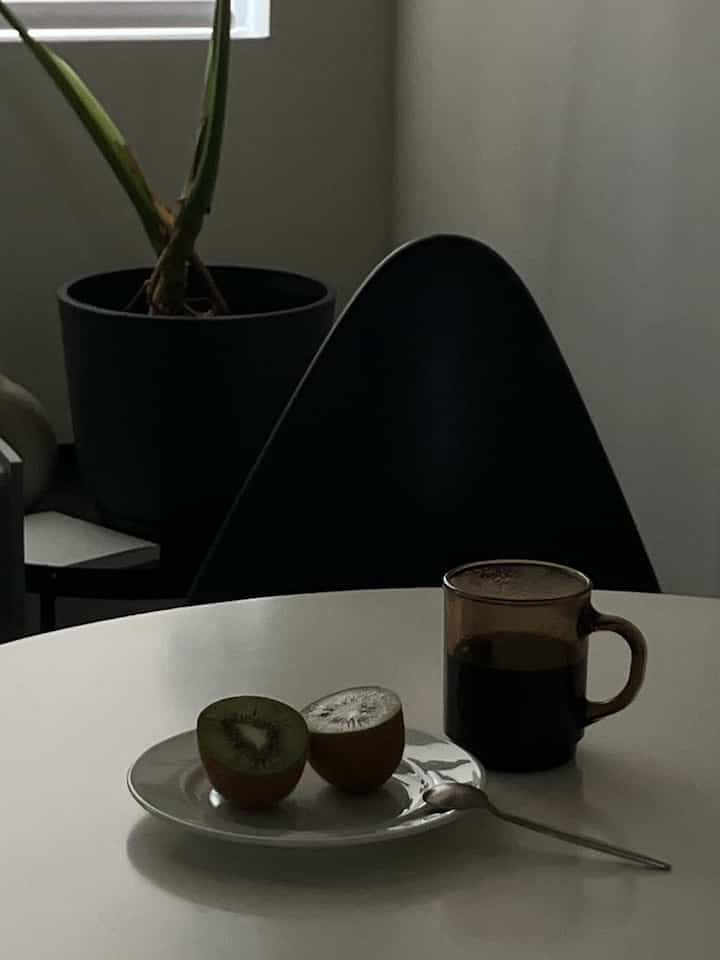 白を基調としたダイニングルーム、中央に白い丸テーブルとシルバーのスプーン、黒い椅子と観葉植物が配置された落ち着いた空間