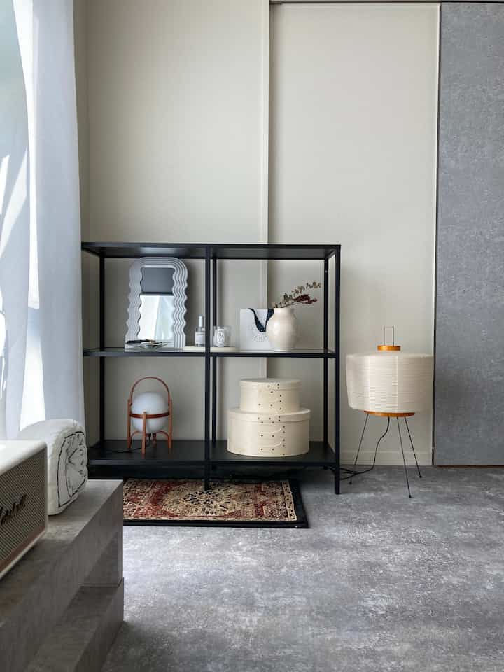 モノトーンのリビングルーム、黒のメタルシェルフとヴィンテージラグ、フロアランプがシンプルな雰囲気を演出