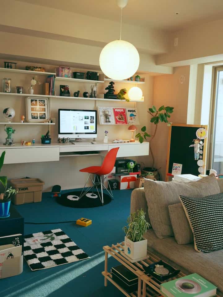 Modern living room and home office with white walls and blue carpet, featuring sofa, desk, and ambient lighting