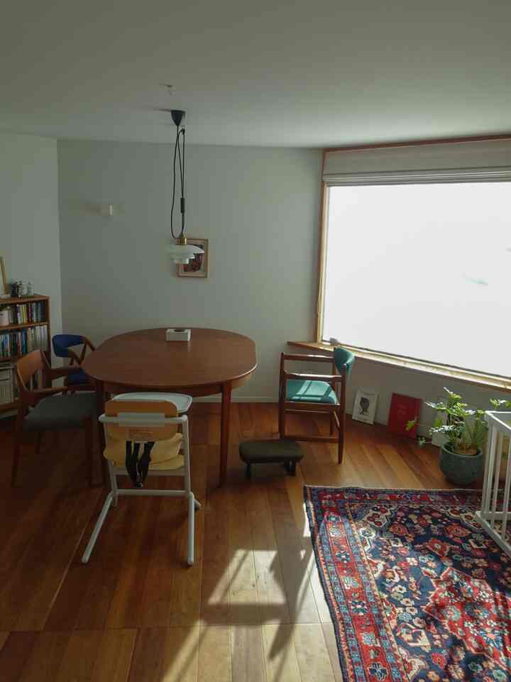 白い壁と木目調の床と家具が調和する北欧風のリビング、ダイニングテーブルと椅子、赤ちゃん用椅子が配置された温かみのある空間