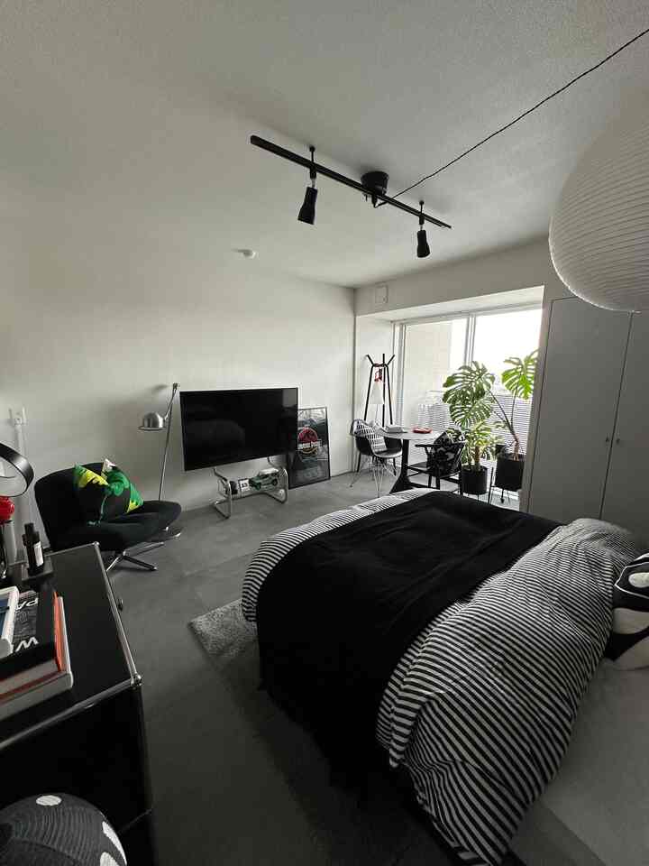 Bedroom with white walls and ceiling, black bedding and armchair, featuring plants and round desk near window in a modern setting