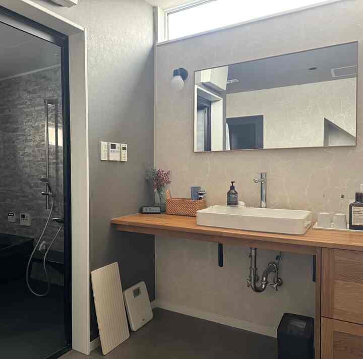 ナチュラルな色調のバスルーム、木製カウンターと大きな長方形の鏡が配置された清潔感のある空間