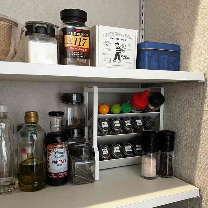 白い棚に透明な容器が並べられ、調味料やスパイスが整然と収納された清潔感のあるキッチンの空間