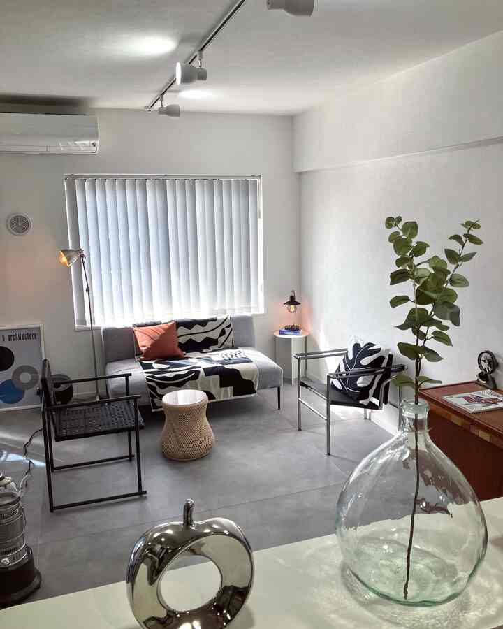 Simple living room featuring a gray sofa, black chairs, white walls, and natural light from a window with vertical blinds
