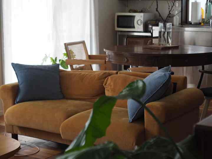 ブラウンの木目調とマスタード色のファブリックソファが中心のリビング、木製のダイニングテーブルとラタンチェアが配置された自然で雰囲気のあるヴィンテージ風インテリア