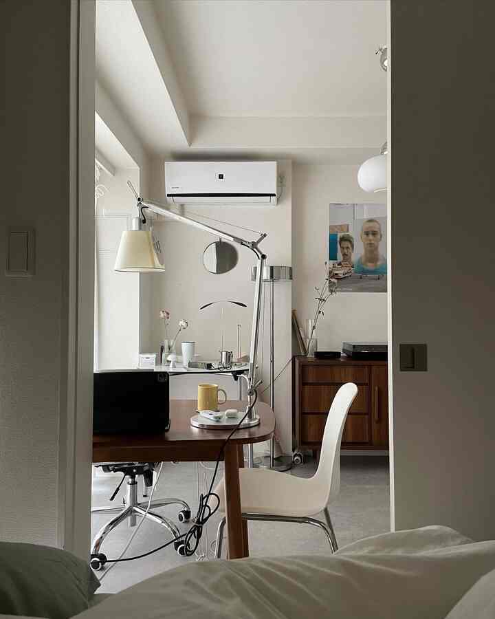 ホワイトとウッドトーンが調和した寝室兼ホームオフィス、シンプルでモダンな家具と照明が配置された落ち着いた印象の空間