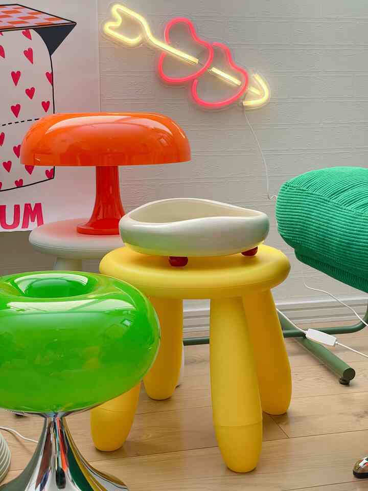 鮮やかな黄色、オレンジ、緑を基調としたレトロスタイルの空間に、ユニークなスツールと大きなキノコ型テーブルランプが配置された可愛らしいスペースエイジインテリア