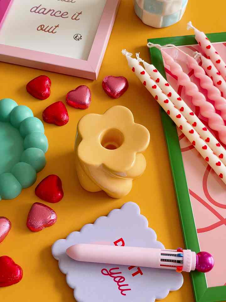 A cozy interior setup with pink and white heart-patterned candles and flower-shaped candle stand on a yellow background