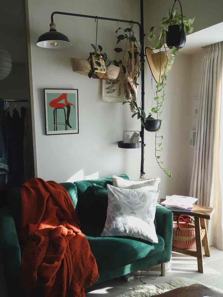 緑のベルベットソファとオレンジのブランケット、サイドテーブルや植物が配置された雰囲気のあるリビング