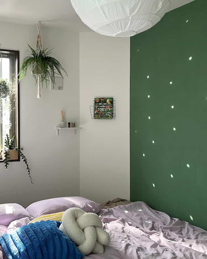 白と緑の壁が特徴の寝室、ラベンダー色の寝具と植物が配置された自然な北欧風のインテリア