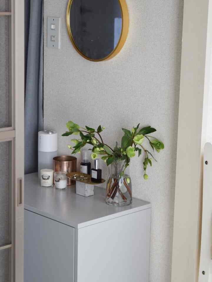 落ち着いたアイボリーとホワイトの玄関空間、ドレッサーの上に緑のクリスマスローズとキャンドル、ディフューザーが置かれた雰囲気のあるインテリア