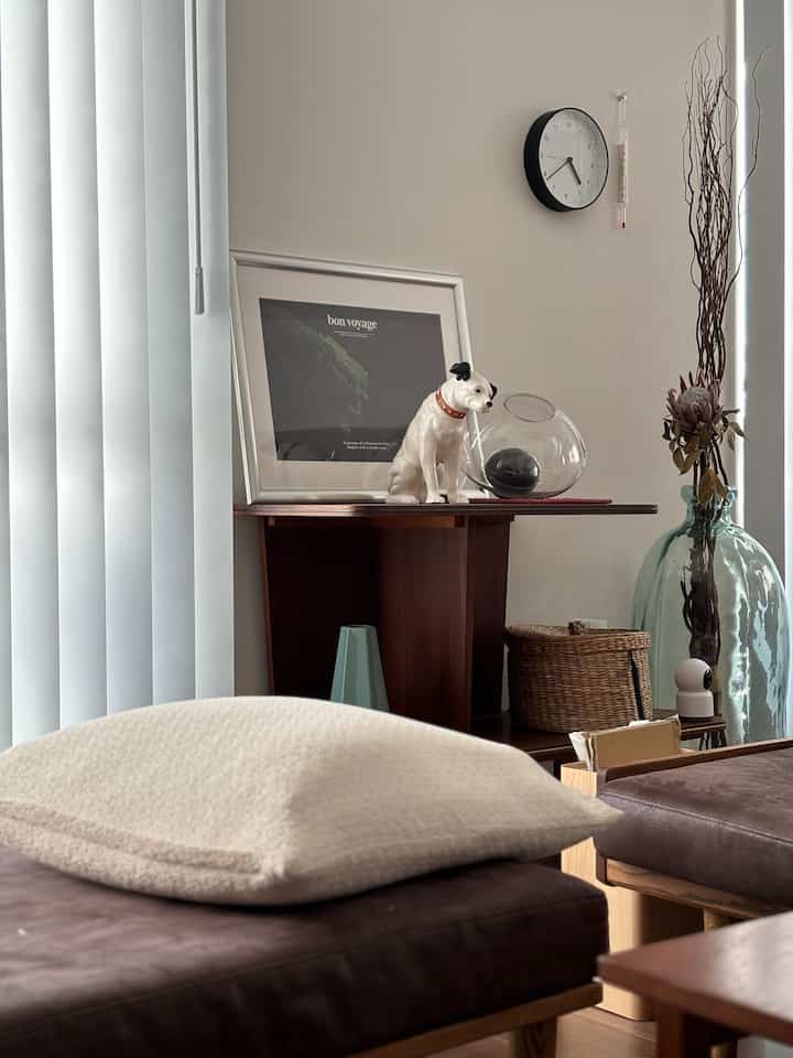 白いブラインドとチャコールのクッションがあるミッドセンチュリーモダンのリビング、自然の装飾と犬の置物が調和した雰囲気あるインテリア