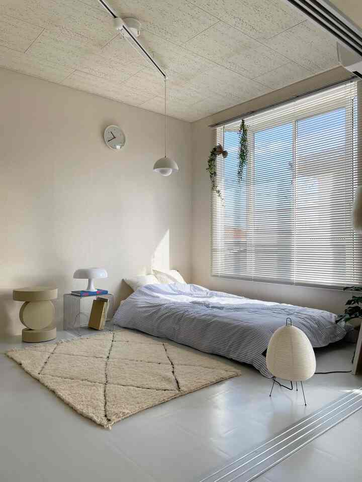 Beige and natural tone bedroom featuring a floor-level bed, a stool, pendant light, and blinds creating a cozy atmosphere