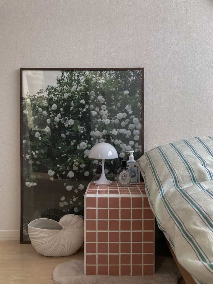 Beige wall bedroom featuring a tiled side table, bed with striped bedding, and a large floral poster creating a cozy single space