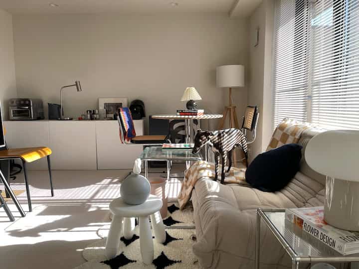 ホワイトとベージュの色調のリビング、ナチュラルモダンなソファとスツール、犬がいる温かみのある空間