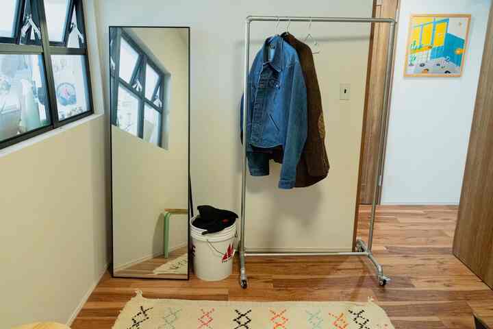 白い壁とナチュラルな茶色の床の廊下、スタンドミラーと移動式の洋服掛けが配置されたミニマルな雰囲気のインテリア