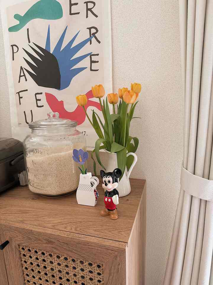 明るい木目調のキャビネットの上に白い花瓶とオレンジのチューリップが置かれた北欧風の玄関スペース