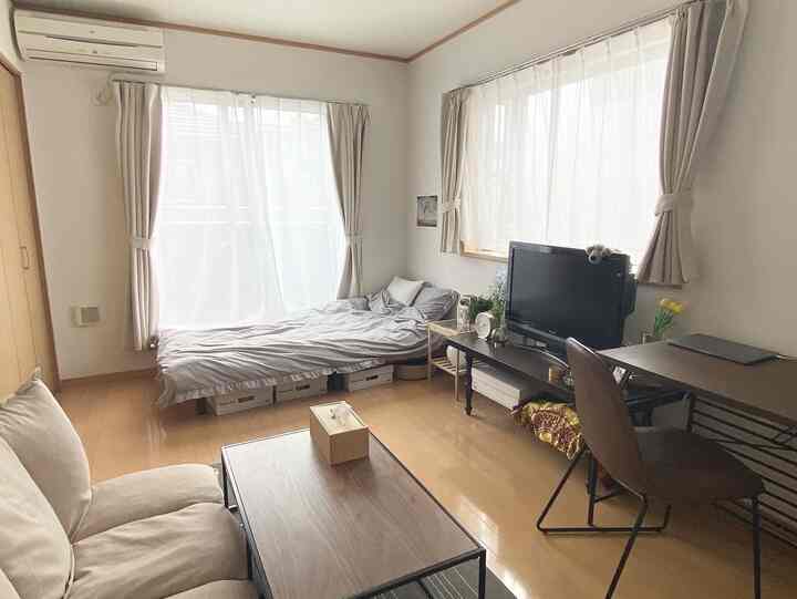 White-walled, brown-floored single household bedroom living room featuring sofa, bed, and desk in a cozy layout