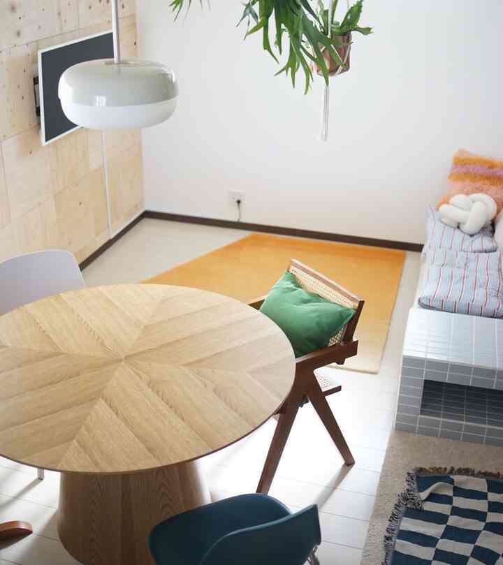 ホワイトを基調とした木目調の丸テーブルと椅子、オレンジ色のラグとクッションが配置された落ち着きのあるリビングスペース