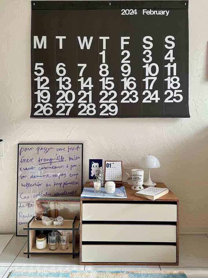 Beige and black toned living space with a large wall calendar and organized storage cabinet, neat and minimalist interior