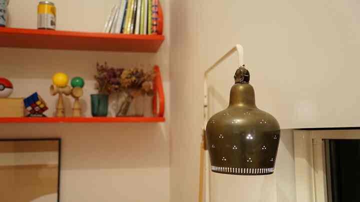 ゴールドブラスの壁掛け照明と鮮やかなオレンジ色の壁棚が配置されたワークスペースのインテリア