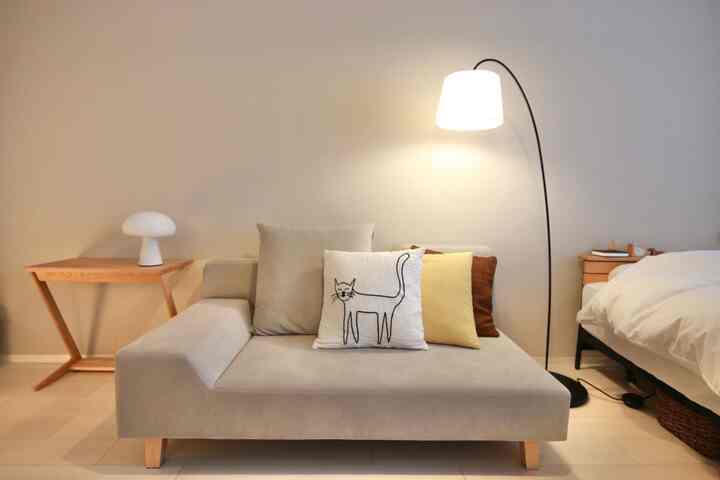 ベージュ調のリビング空間、猫の絵柄クッションを置いたソファとアーチ型のフロアランプ、木製サイドテーブルが配置された温かみのあるインテリア