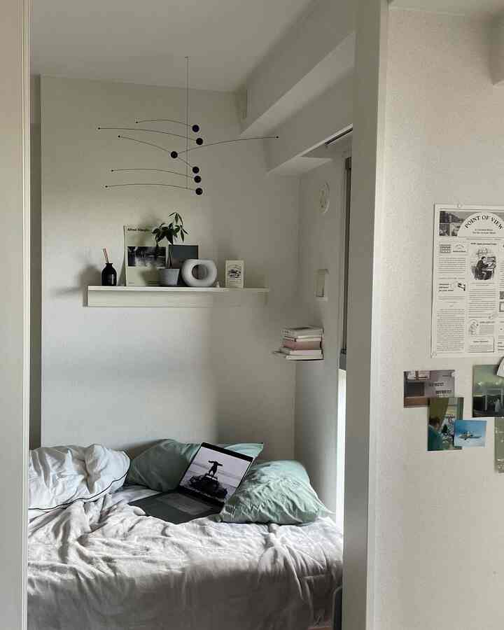 白と淡い緑のトーンの小さな寝室、壁の棚とモビールが配置された落ち着いたシンプルなインテリア