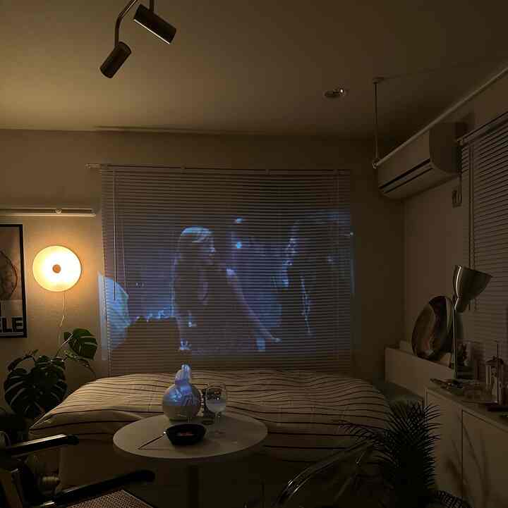 白とナチュラルカラーの小さな寝室、ブラインドに映画が映し出されている雰囲気のあるホームシネマ空間