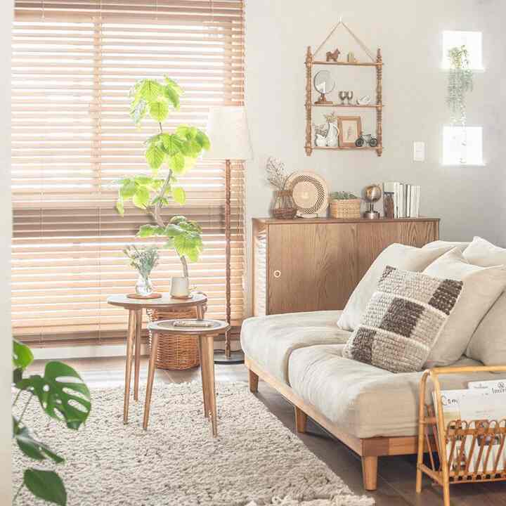 ナチュラルな木目調とベージュのソファ、ラグが配置された明るい木製ブラインドのある居心地の良いリビング