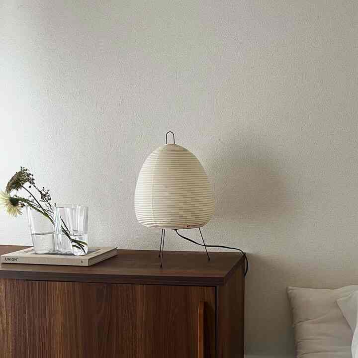 Natural and simple studio apartment featuring white walls, a brown wooden cabinet, and a round paper shade table lamp