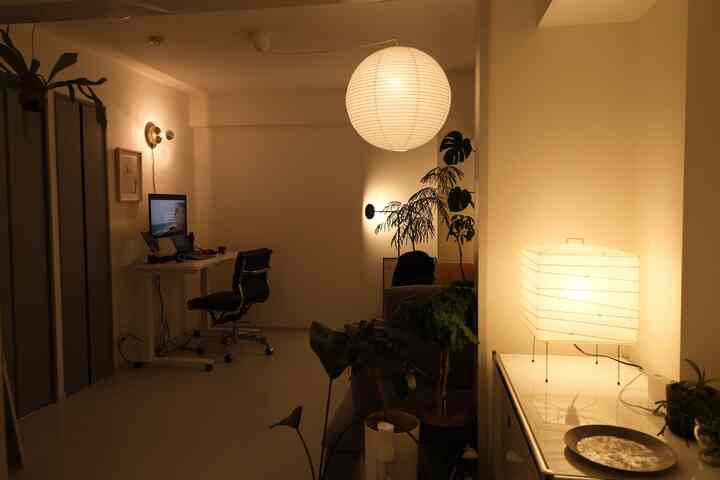 暖かなイエローライトのホームオフィス、天井のペンダントライトとデスク、植物が配置されたナチュラルで落ち着いた雰囲気の空間