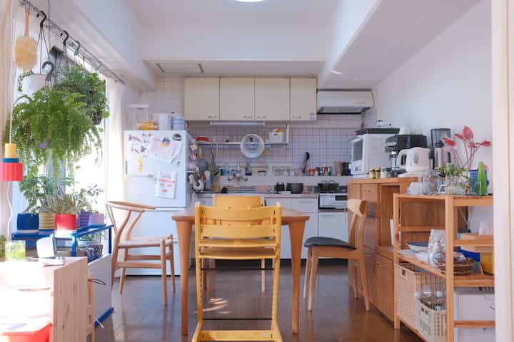 白と木目調が調和したキッチン兼ダイニングスペース、食卓と椅子、多彩な観葉植物が配置された雰囲気のあるインテリア