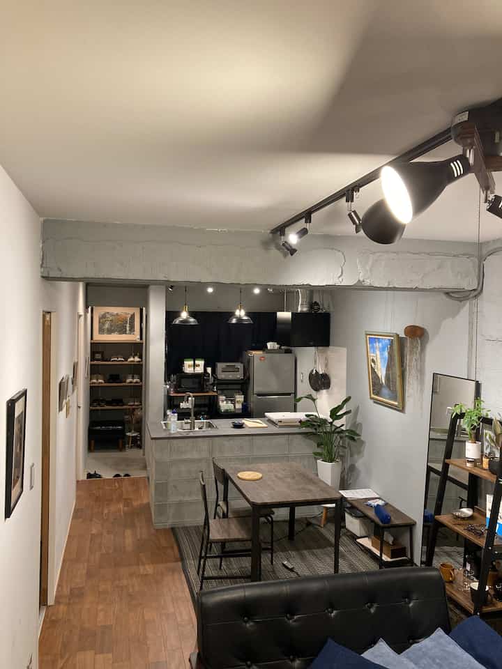 モダンなグレーとブラックのトーンが特徴のワンルームリビングとキッチン、木目調のダイニングテーブルとラグが調和した印象的な空間