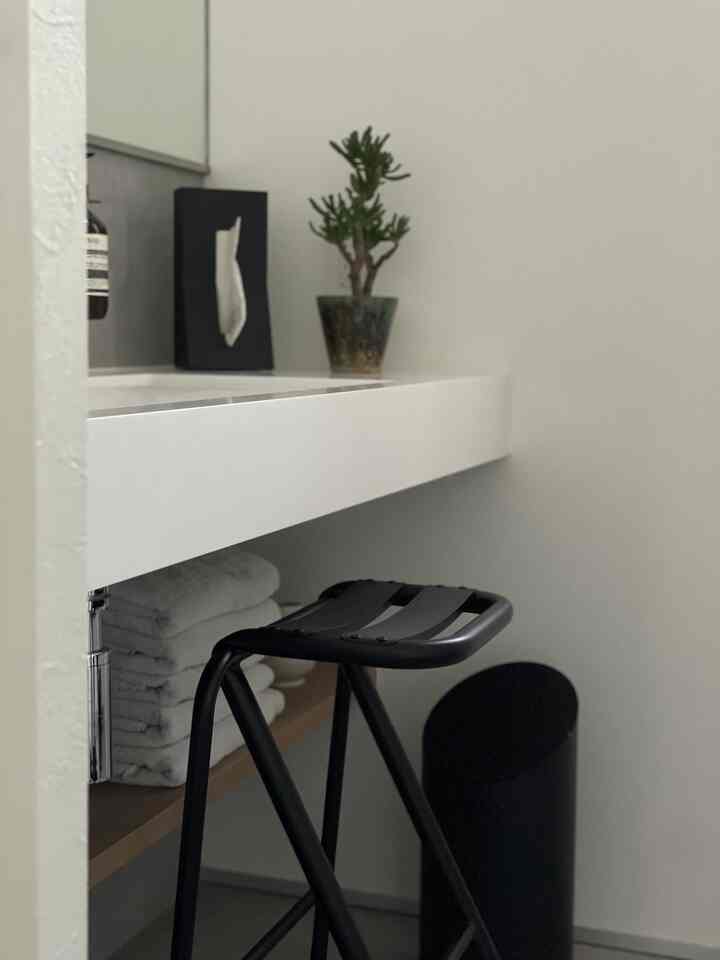 白と黒のトーンのパウダールーム、白い洗面台と黒いスツール、観葉植物が配置されたシンプルな空間