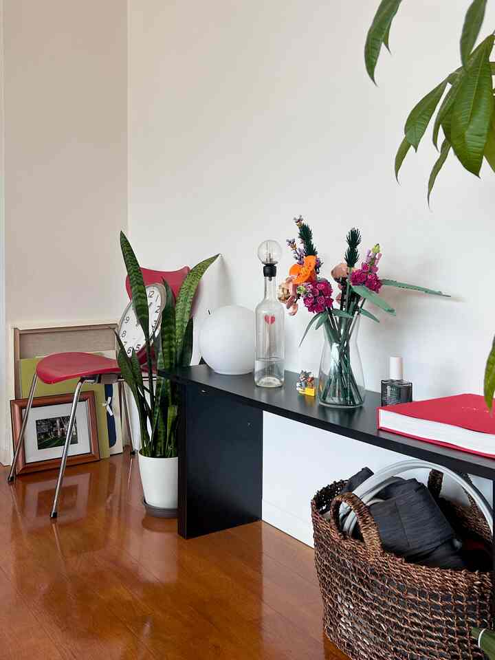 ブラウンの木製フローリングと白い壁が調和するリビングの一角。黒いコンソールテーブルには花瓶や小物、赤い椅子が配置された落ち着いた空間。