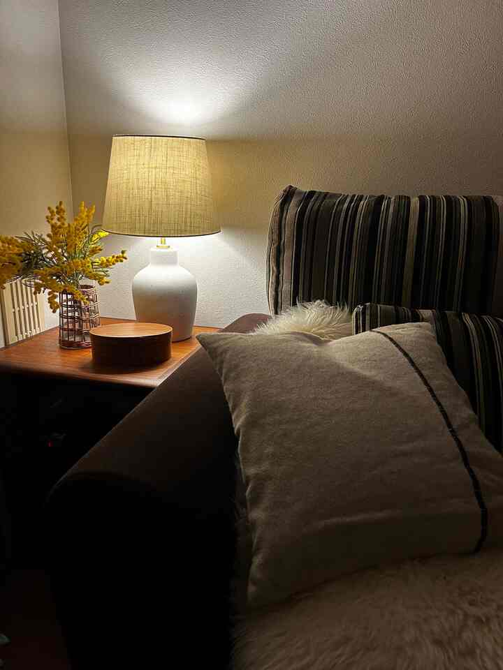 暖かいベージュとブラウンの色調のリビング、ソファとサイドテーブルの上に灯りのともったテーブルランプが配置された印象的な空間