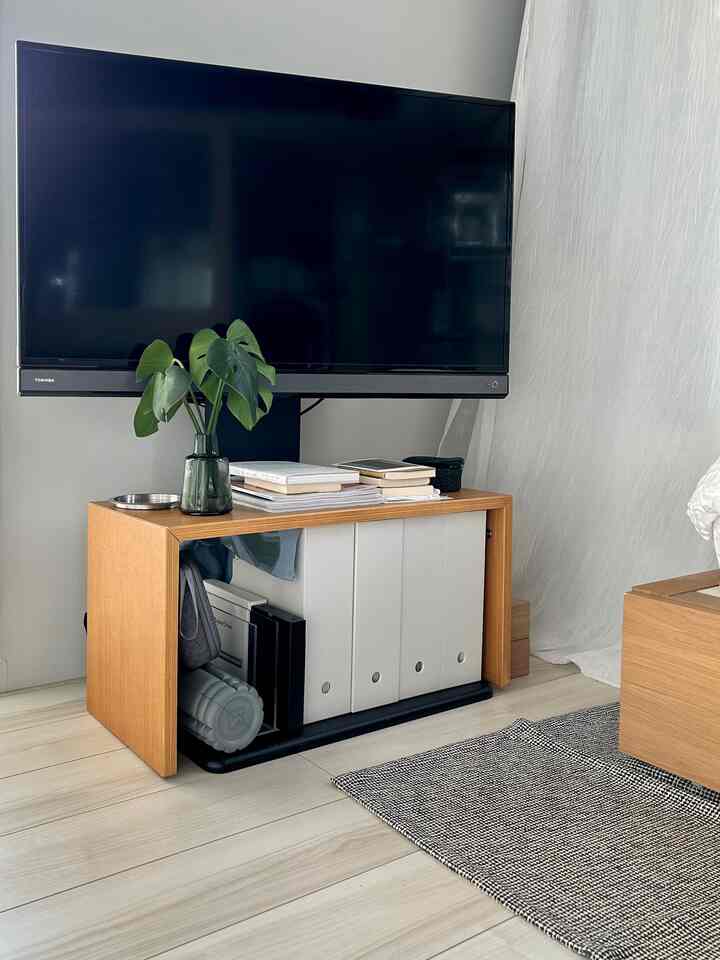 ナチュラルな木目と白い壁のワンルーム、無印良品のコの字テーブルとニトリのテレビ台が配置された印象的な空間