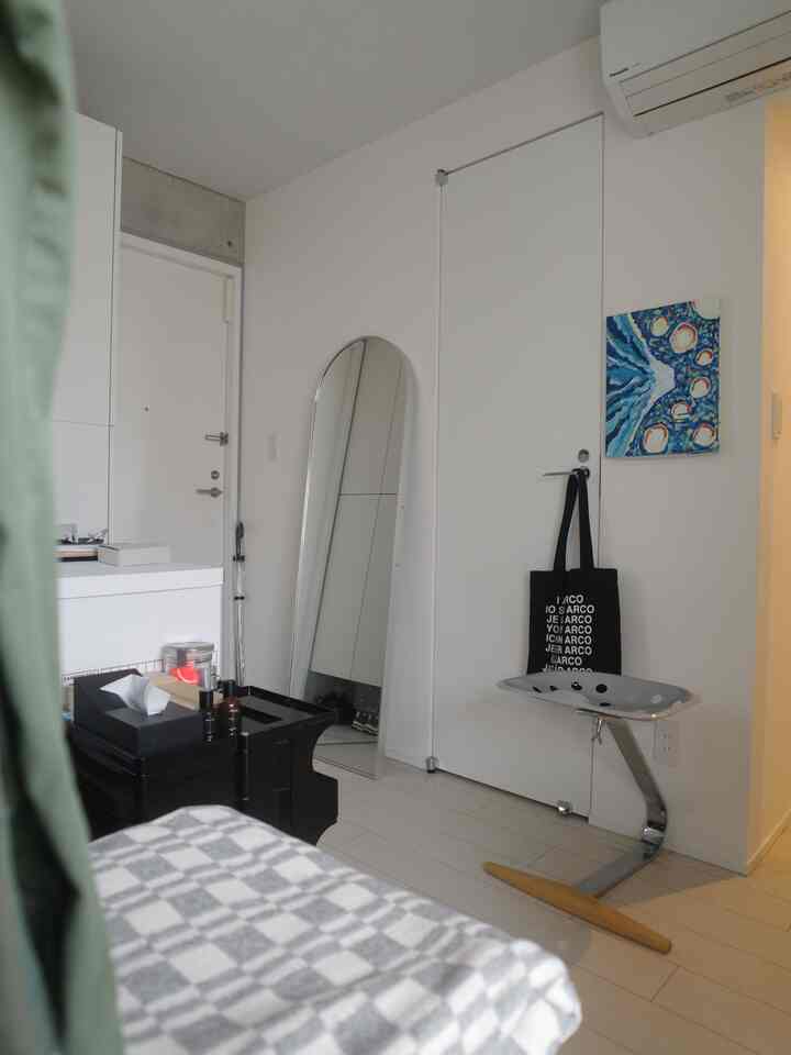 Modern entrance space in white tones featuring a silver stool, arched full-length mirror, and wall art painting