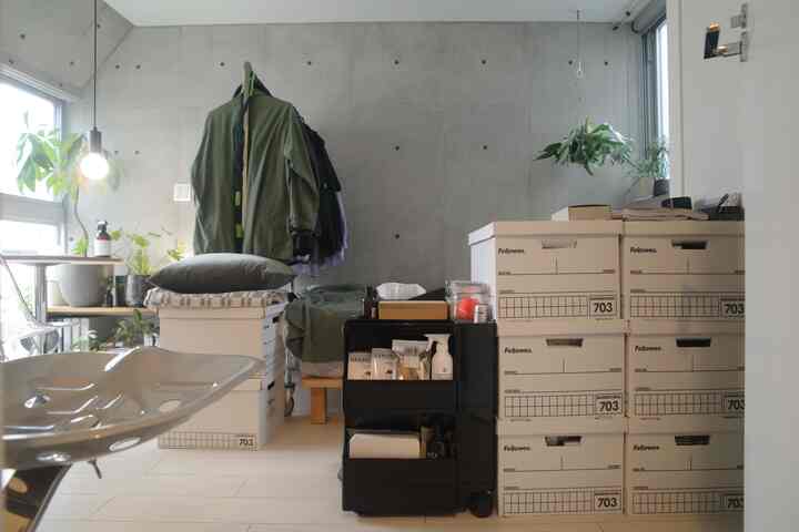 ベージュトーンの収納ボックスとモダンなコンクリート壁のリビングの一角、整理された箱と植物が配置された印象的な空間