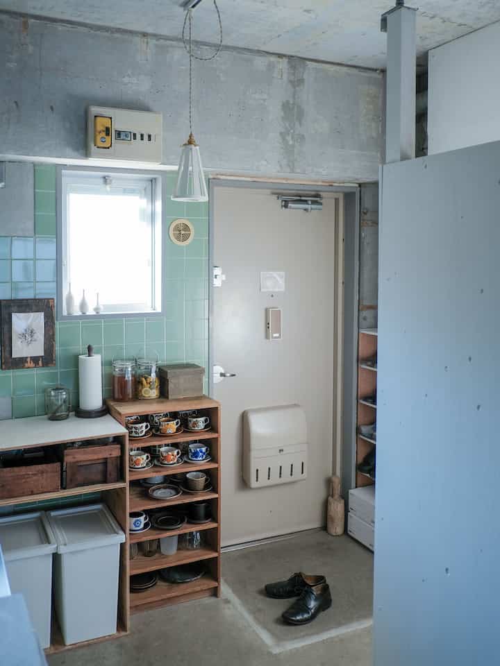 A narrow entrance space featuring green tiled walls and natural wood storage shelves with a vintage vibe