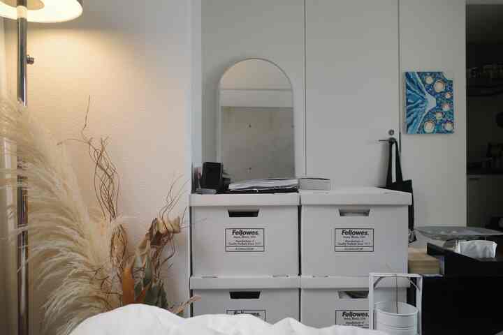 白を基調とした寝室の一角、ドライフラワーと白い収納ボックス、アーチ型の鏡が配置された雰囲気のあるインテリア