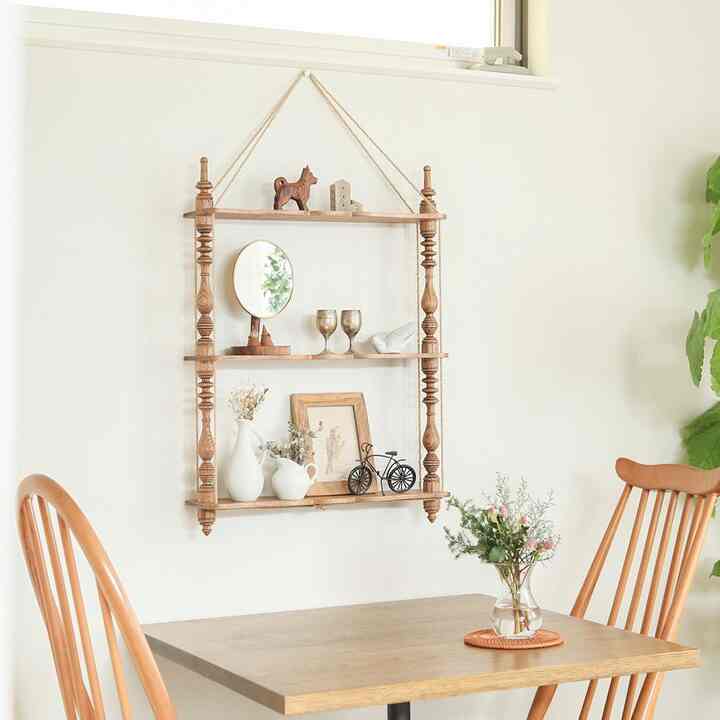 白い壁と茶色の木製テーブル、椅子があるカフェ風の空間、壁の棚に様々なオブジェが配置された落ち着いた雰囲気のインテリア