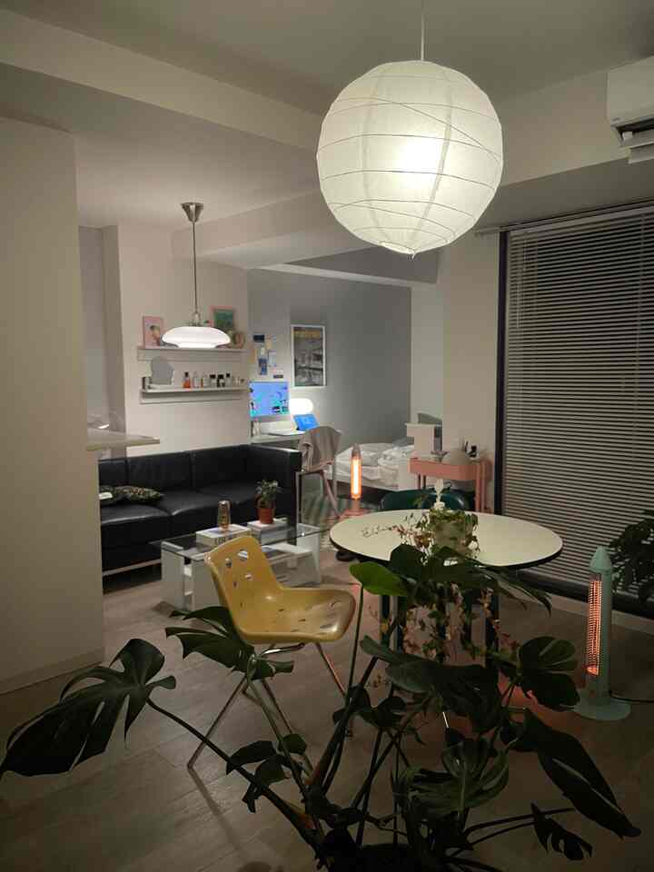 Simple modern studio apartment living room with white walls and black leather sofa, featuring a home office space and round dining table for a cozy atmosphere