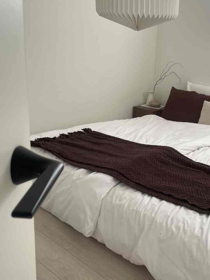 White and brown toned bedroom featuring a centrally placed bed with pillows and a brown bedspread, creating a clean and cozy atmosphere