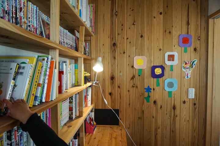 Natural-toned kids' room featuring wooden walls, bookshelf filled with books, and origami flower decorations on the wall creating a cozy atmosphere
