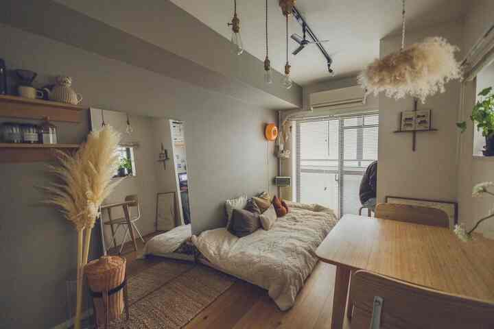 ナチュラルな色調と木製家具が配されたワンルーム、壁際の大型鏡とブラインドが開放感を演出する温かみのあるインテリア